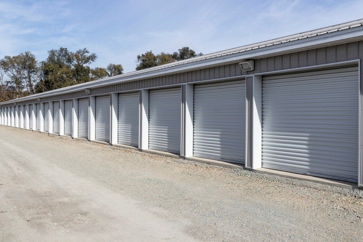 Row of closed storage unit doors in a gravel lot in Capitol, CA